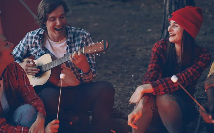 Friends round a campfire with a guitar